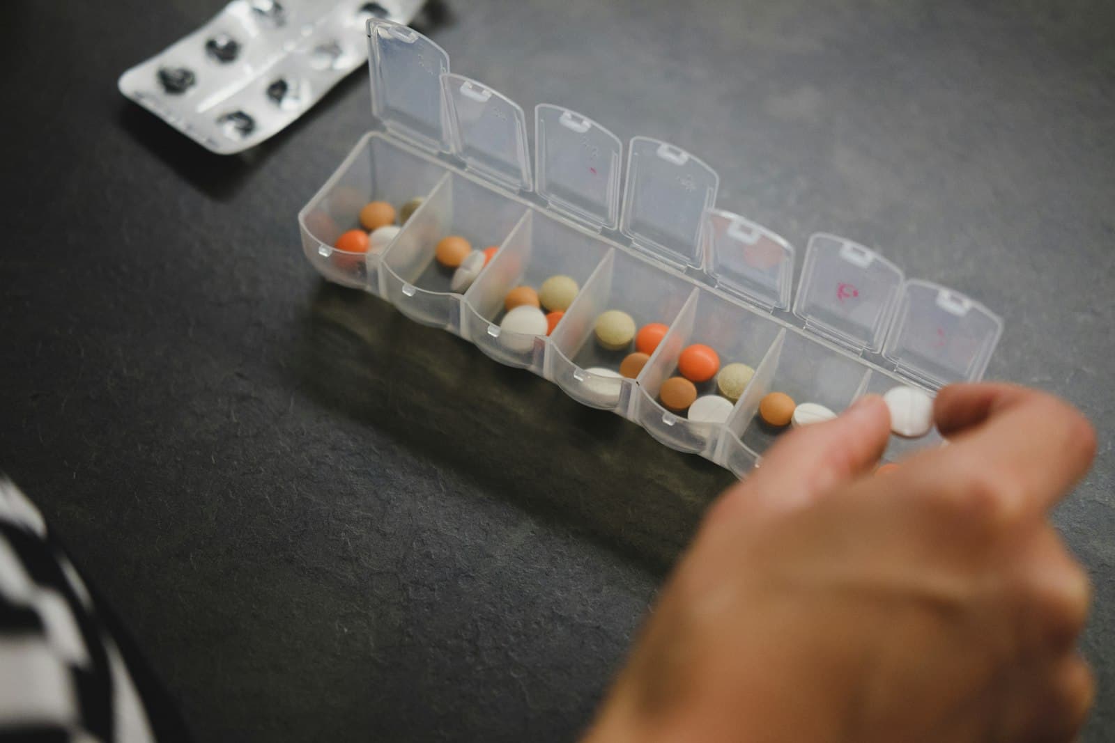 A weekly pill organizer being filled on a table.